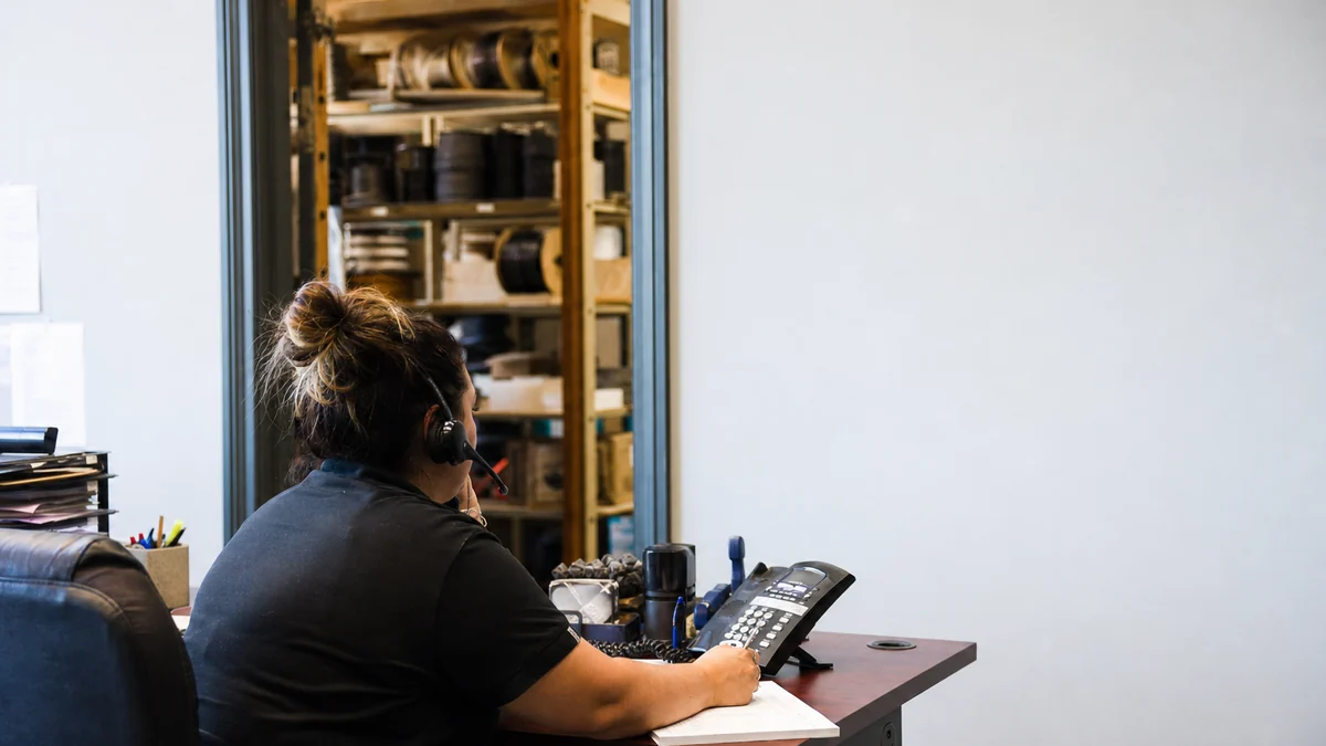 Office manager at an electrical shop taking a customer call and writing up a job ticket