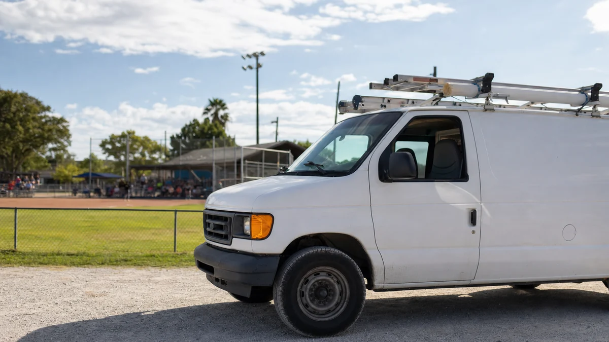 HVAC service van parked beside a local youth baseball field on a sunny afternoon
