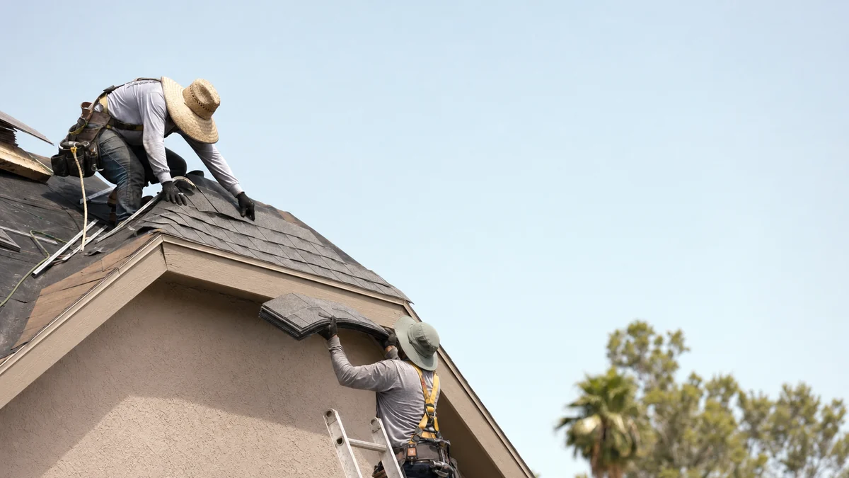 Two roofers laying shingles on a residential roof